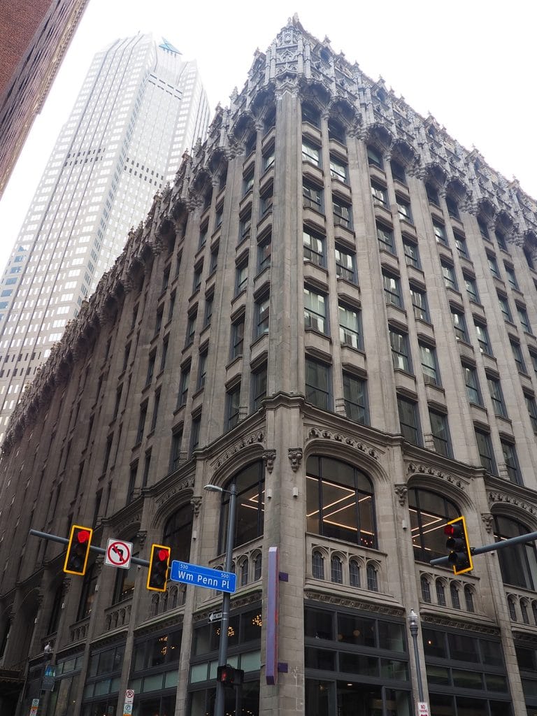 a photo of an ornate high-rise building rising up above a street corner traffic light, with a much larger skyscraper towering in the background