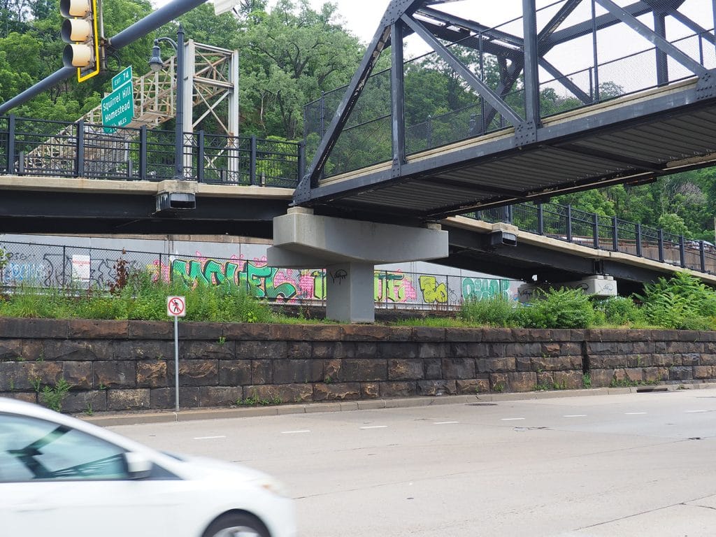 a photo of a pedestrian bridge over a road, with a graffiti-covered concrete wall visible behind