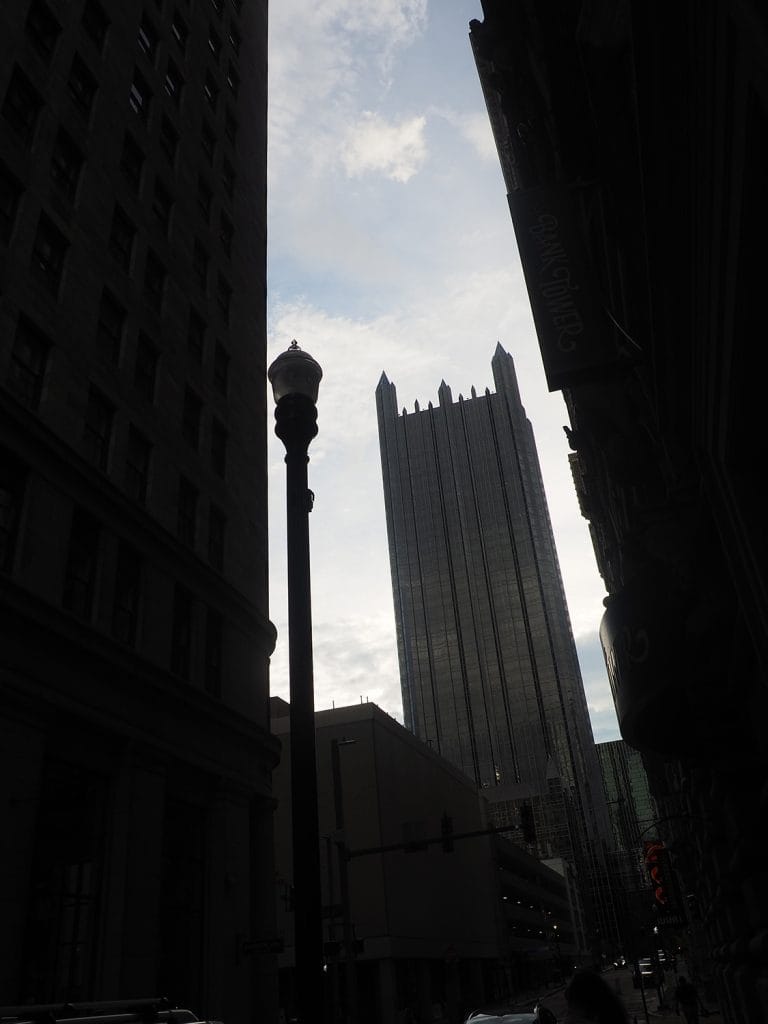 a photo of an ornate skyscraper, dark against a bright daytime sky, framed by even darker skyscrapers