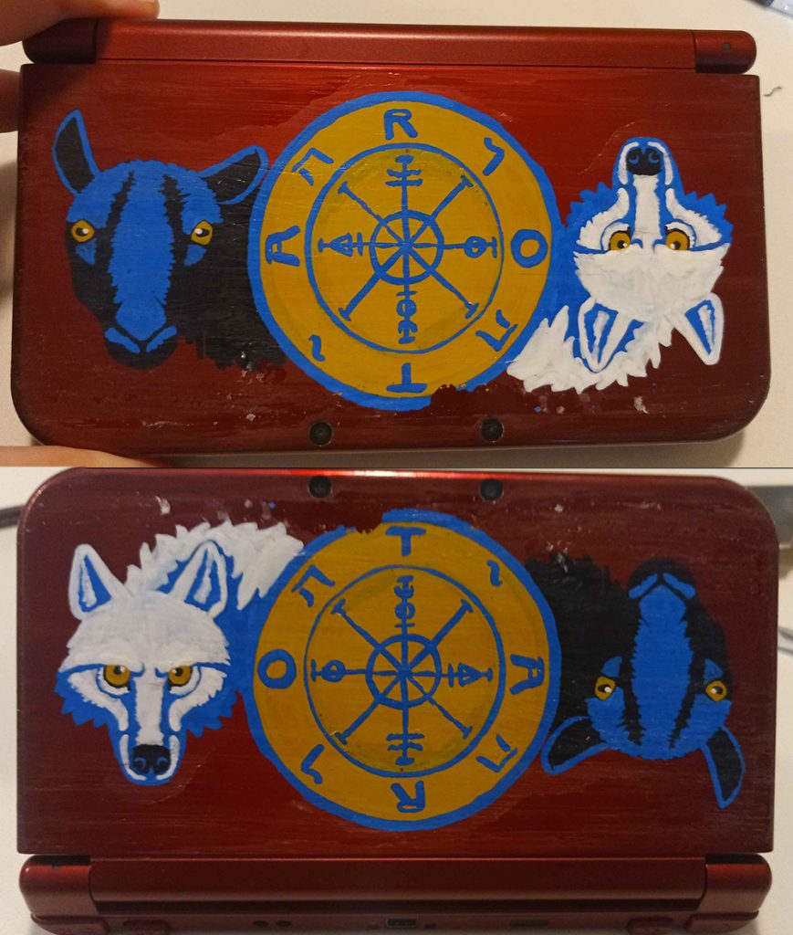 two photographs of a red Nintendo 3DS XL with a design drawn on it. the design is blue, white, black, and gold, and depicts a white wolf and a black sheep emerging from behind either side of the Rider-Waite tarot's Wheel of Fortune. the design is reversed in each photograph, with either the wolf or the sheep facing correctly and the other appearing upside-down