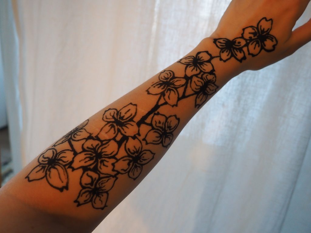 photograph of a forearm with dogwood blooms drawn on it in black henna